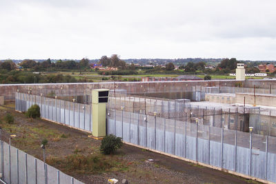 A photograph taken by Rab Kerr who was an Open University student in the Republican Wings of the H Blocks. It shows the Maze and Long Kesh Prison site in 2005. It is taken from a high vantage point and shows a watch tower in the middle of frame and two rows of tall security fences between prison buildings (H Blocks).